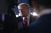 Donald Trump står utendørs foran sterke lys ved et fly og snakker med pressen.