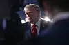 Donald Trump står utendørs foran sterke lys ved et fly og snakker med pressen.