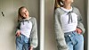 To barn i hvite topper, jeans og lyse, fluffy cardigans står ved en vegg.