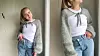 To barn i hvite topper, jeans og lyse, fluffy cardigans står ved en vegg.