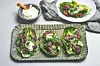 Fire salatblader med kjøtt og grønnsaker på et fat, med en skål dressing ved siden av.
