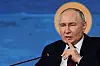 Vladimir Putin sitter ved en mikrofon og gestikulerer under et forum på en scene med blå bakgrunn.
