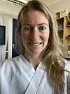 Person i hvit uniform står innendørs foran hyller og et vindu.