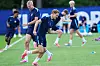 Flere norske fotballspillere trener på en gressbane med kjegler og blå treningsutstyr.