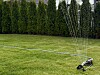 Sprinkler som vanner grønn plen foran en tett hekk i en privat hage.