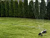 Sprinkler som vanner grønn plen foran en tett hekk i en privat hage.