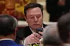 Elon Musk sitter ved et bord og bruker mobiltelefon under en statsbankett i Beijing.