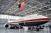 Et Air Force One-fly står i en lys hangar med amerikansk flagg og personer ved understellet.