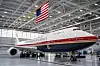 Et Air Force One-fly står i en lys hangar med amerikansk flagg og personer ved understellet.
