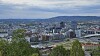 Panoramautsikt over storby med elv, broer og bygg, sett fra et grønt utsiktspunkt.
