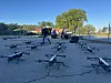Rekke med droner på asfalt mens personell tester utstyr i bakgrunnen på Fort Stewart.