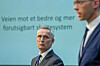 Eigil Knutsen og Jens Stoltenberg foran en blågrønn bakgrunn under presentasjon av skatterapporten.