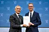 Skattekommisjonens leder overrekker en rapport til finansminister Jens Stoltenberg foran blå bakgrunn.