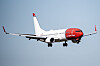 Et Norwegian-passasjerfly med rød nesedel og landinghjul ute flyr mot kameraet.