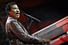Lionel Richie synger ved et rødt piano på en scene med mikrofon.