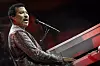 Lionel Richie synger ved et rødt piano på en scene med mikrofon.