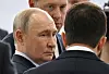 Vladimir Putin står i forgrunnen mens han ser mot flere personer ved en flyutstilling innendørs.