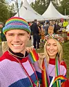 Bildet viser en fargerik heklet Elton hatt i regnbuestriper, brukt på festival sammen med strikkede plagg i sterke farger. Bildet passer godt til en artikkel om gratis hekleoppskrift på sommerlig bøttehatt, og viser hvordan hatten kan bli et tydelig tilbehør til festival, Pride og andre sommerarrangementer.