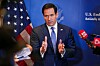 Marco Rubio står foran et amerikansk flagg og svarer på spørsmål fra journalister med mikrofoner.