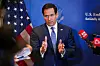 Marco Rubio står foran et amerikansk flagg og svarer på spørsmål fra journalister med mikrofoner.