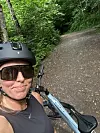 Syklist i hjelm tar selfie ved en sykkel på en grussti i skogen.