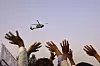 Folk rekker hendene i været mot et helikopter som flyr over Kabul og slipper blomster.