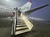Passasjerfly på flyplass med trapp opp til døren i tåke.