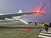 Et fly på en flyplassrullebane i skumring med bakkemannskap og noen personer ved trappen.