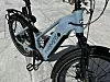 Lys blå elektrisk sykkel med Momas-logo parkert på steinlagt fortau.