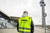 Streikevakt i gul refleksvest står ved Oslo lufthavn Gardermoen med terminal og tårn i bakgrunnen.