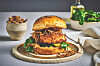 En hamburger med sprø kylling, grønn salat og løk på en tallerken. Sprø panert kylling, mykt briochebrød og kremet dressing gjør denne burgeren saftig, sprø og full av smak. Denne oppskriften på crispy kyllingburger med fritert løk gir en hjemmelaget kyllingburger der både kylling og løk friteres gyllent og sprøtt. Dressingen gir sødme, salt og mild varme. Dette passer perfekt når du vil lage en skikkelig burger med ekstra sprøhet.