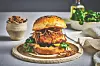 En hamburger med sprø kylling, grønn salat og løk på en tallerken. Sprø panert kylling, mykt briochebrød og kremet dressing gjør denne burgeren saftig, sprø og full av smak. Denne oppskriften på crispy kyllingburger med fritert løk gir en hjemmelaget kyllingburger der både kylling og løk friteres gyllent og sprøtt. Dressingen gir sødme, salt og mild varme. Dette passer perfekt når du vil lage en skikkelig burger med ekstra sprøhet.