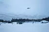 Helikopter flyr over et snødekt landskap med soldater og skog i Troms under vintertrening.