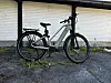 Lysgrønn elsykkel står parkert mot en hvitmalt vegg på asfalt.