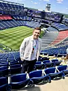 Mats Arntzen står foran blå stadionseter med utsikt over en tom fotballbane og fargerike tribuner.