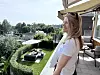 En kvinne står på en terrasse og ser ut over en grønn hage med utemøbler og parasoll.