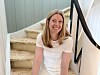 Smilende kvinne i hvit topp sitter på en innendørs trapp.