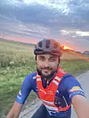 Jonas Andersen Sayed i sykkelklær og hjelm tar et selfie-bilde på en landevei ved solnedgang.