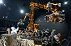 Stor robotarm og utstyr i en mørk romsimulator med blanke overflater og testoppsett.