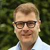 Mann med svarte briller og lys skjorte foran uskarp grønn bakgrunn.