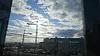 Bylandskap med kraner, kontorbygg og lysende skyet himmel sett gjennom et vindu.