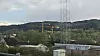 Industriområde med bygninger, master og skogkledd ås i bakgrunnen.