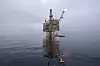 Oljeplattform i havet med flamme på toppen under overskyet himmel.