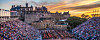 Stor folkemengde sitter på tribunene foran Edinburgh Castle i skumringslys.