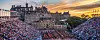 Stor folkemengde sitter på tribunene foran Edinburgh Castle i skumringslys.