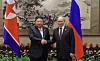 To menn i dress håndhilser foran flaggene til Nord-Korea og Russland i et dekorert møterom.