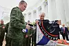 Vladimir Putin holder opp en mørk militærfaneremse under et møte i et lyst rom med flere uniformerte menn.