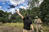 Ukrainsk soldat styrer en FPV-drone utendørs ved frontlinjen, mens en annen soldat står i bakgrunnen.
