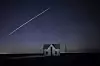 Lang eksponering av Starlink-satellitter over et lite steinhus under stjernehimmel.