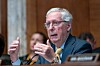 Mitch McConnell sitter ved et bord i en høringssal og snakker mens han gestikulerer.